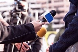 stock image of a reporters holding microphones pointed a person you cannot fully see